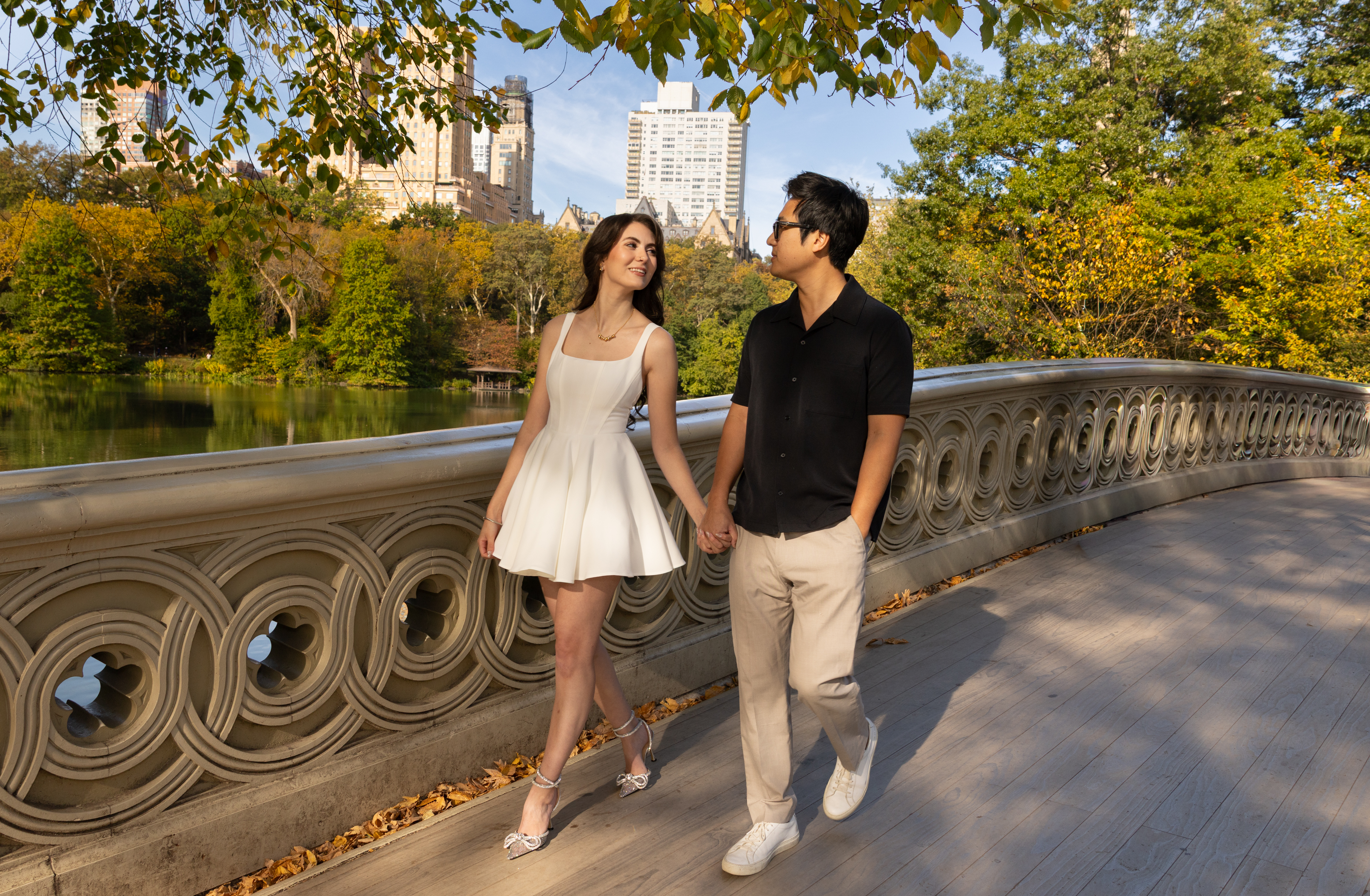 A couple holding hands on a bridge beside a lake and autumn trees